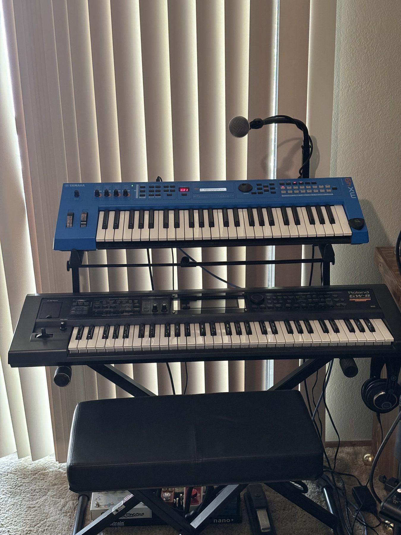 Two keyboards on a rack beside a microphone and piano bench